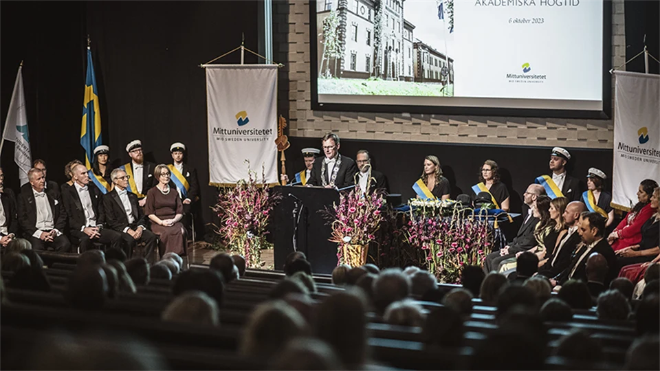 En scen med ceremonideltagare och en man i talarstol. 