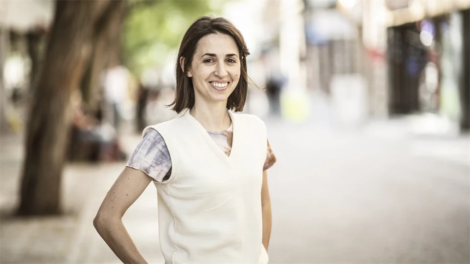 Woman with dark brown hair, patterned short-sleeved blouse and white vest smiling at the camera