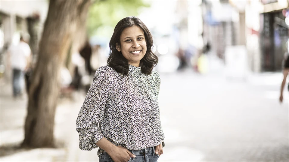 A woman in a patterned blouse and jeans smiles at the camera