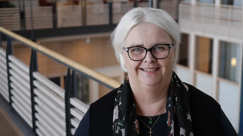 Kvinna står i ljushallen på Mittuniversitetet campus Östersund. Hon tittar in i kameran och ser glad ut.