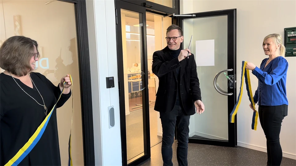 Två personer håller i ett gulblått band som den tredje personen nyss har klippt av.