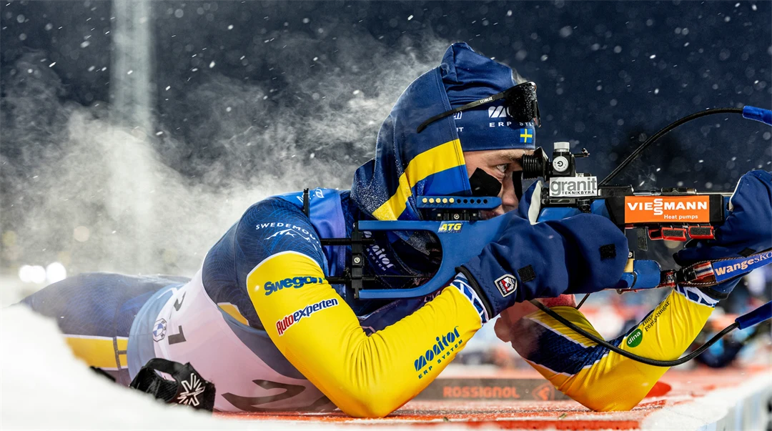 Skidskytt som ligger och siktar med sitt gevär, det ångar från ryggen.