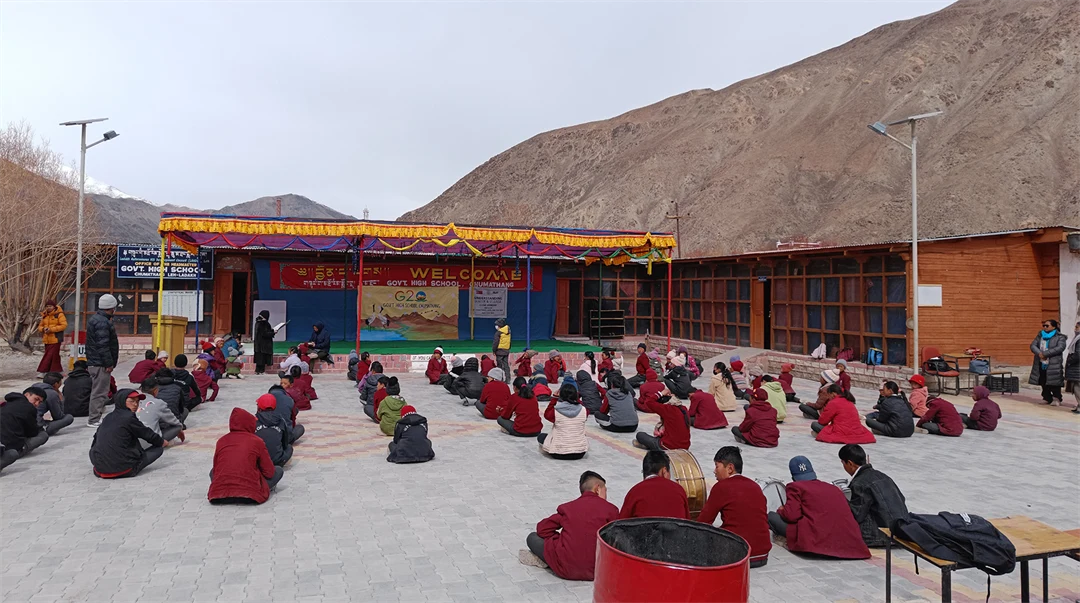 Barn som sitter i rader på marken utanför en låg byggnad.