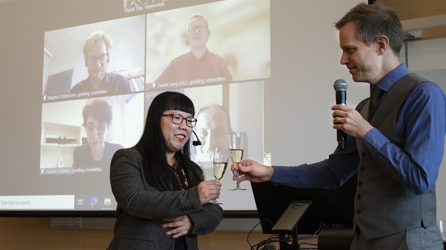 Jan Lundgren and Thanh Tran toast for an approved dissertation. In the background is the examining committee.