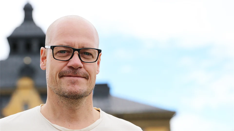 Glasögonprydd man med tak och himmel i bakgrunden.