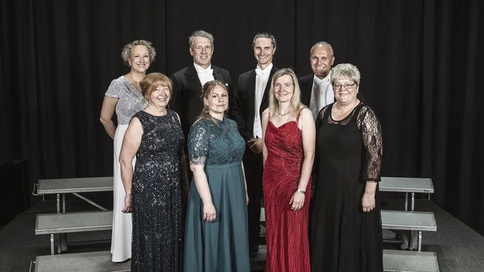 Åtta forskare står tillsammans och poserar för en gruppbild. Alla bär högtidskläder.