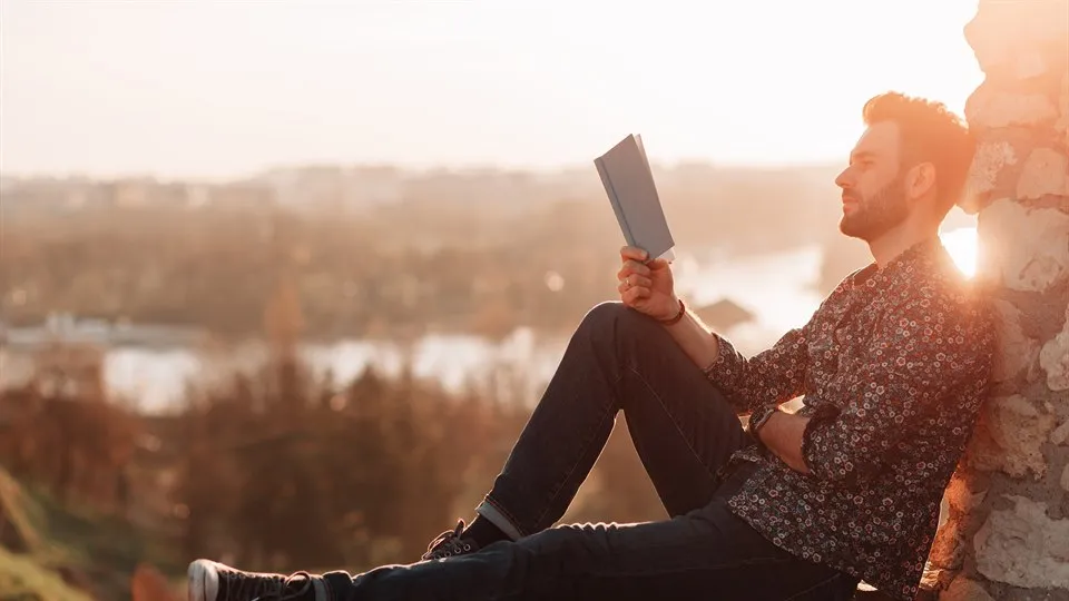 Man läser bok i solen utomhus.