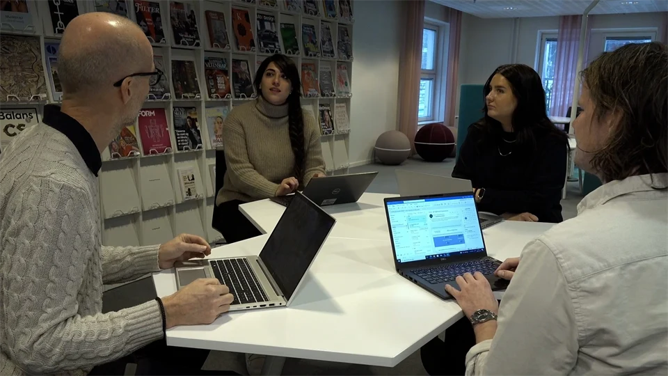 Fyra personer med varsin bärbar dator sitter vid ett bord och samtalar. 