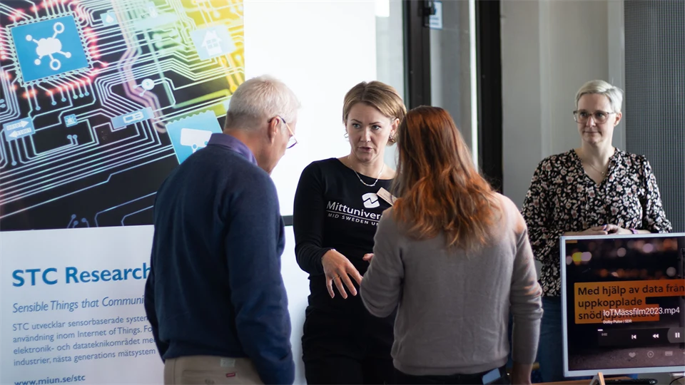 Two women standing and talking to two people. A rollup with the text STC Research next to them. 