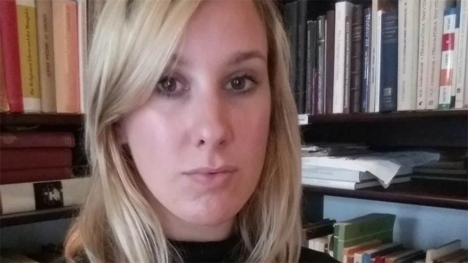 Foto av Anna Ehrhart framför en bokhylla med böcker