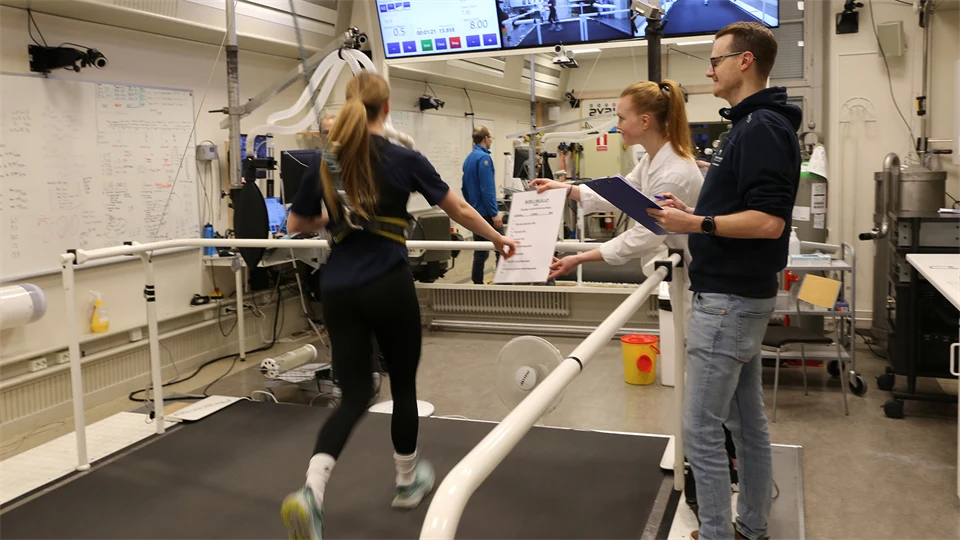 Labbmiljö med en löpare på band och forskare bredvid.