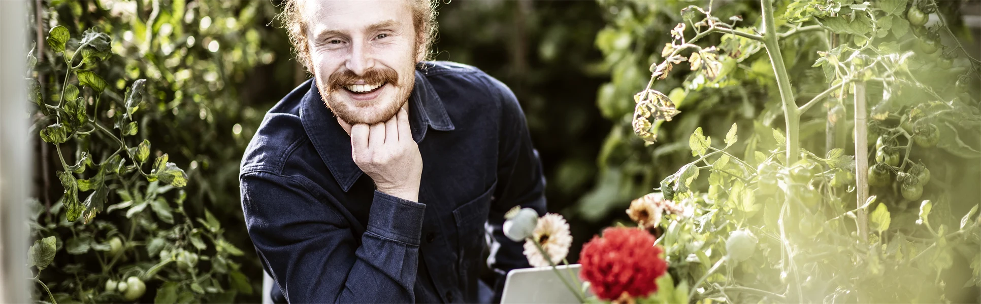 Manlig student sitter i  växthus och pluggar med laptop och böcker. 